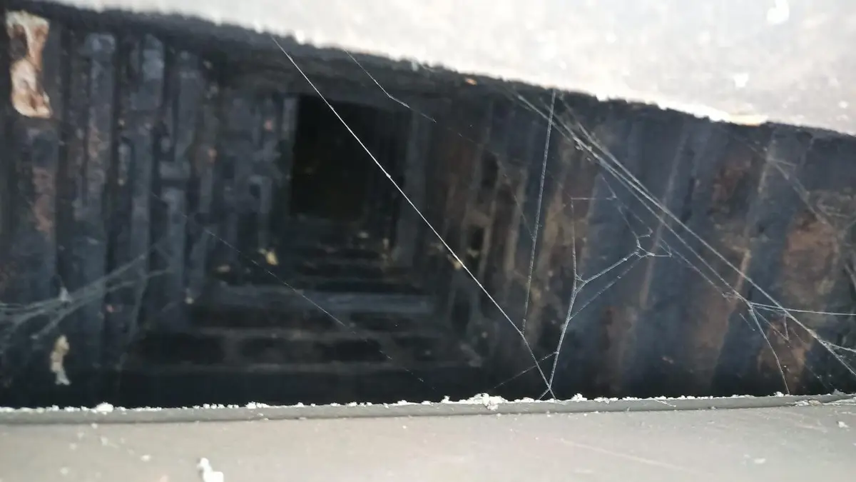 Soot and cobwebs at the damper throat of a fireplace, where summer fireplace smells start