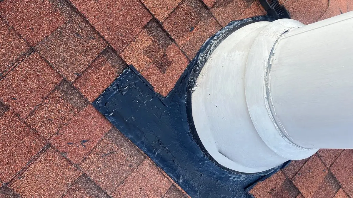 Chimney flashing sealed around a flue pipe on a shingle roof after a leak repair